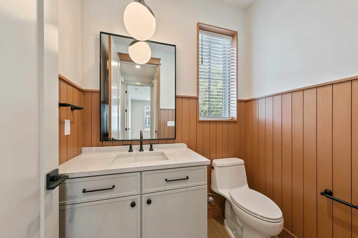 Bathroom with white vanity, toilet, wood paneling, mirror, and a hanging light.