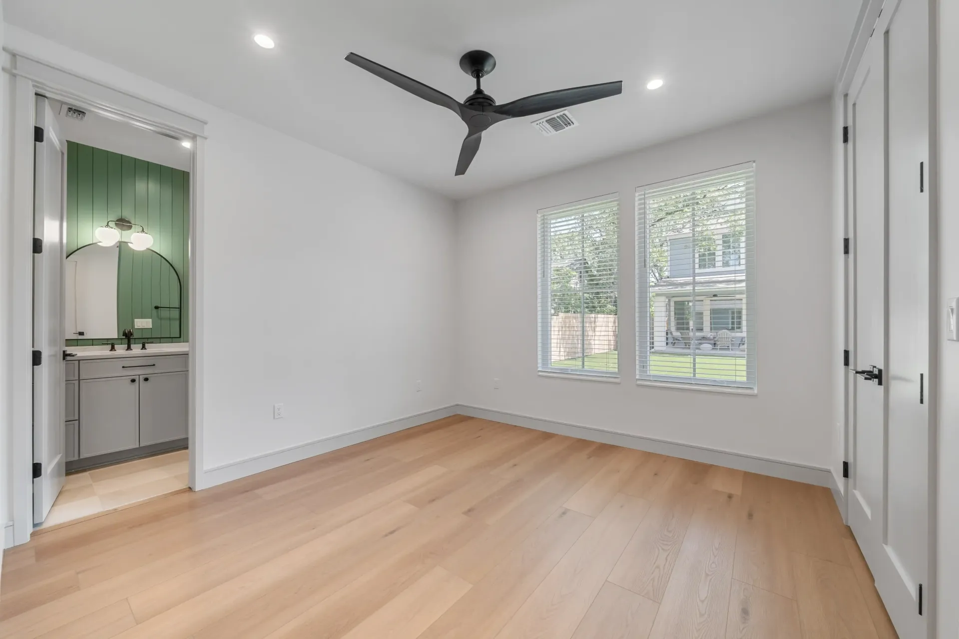 Empty room with wood floors, white walls, two windows, and a bathroom visible.
