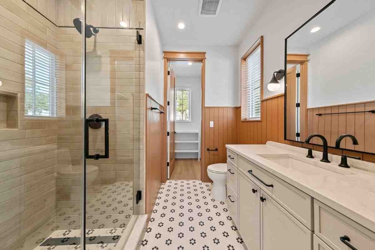 Bathroom with a glass shower, white vanity, patterned floor tiles, and wood accents.