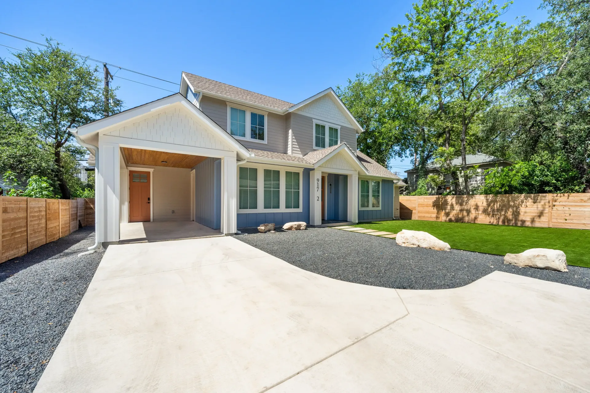 Two-story house with a light gray exterior, carport, and landscaped front yard.
