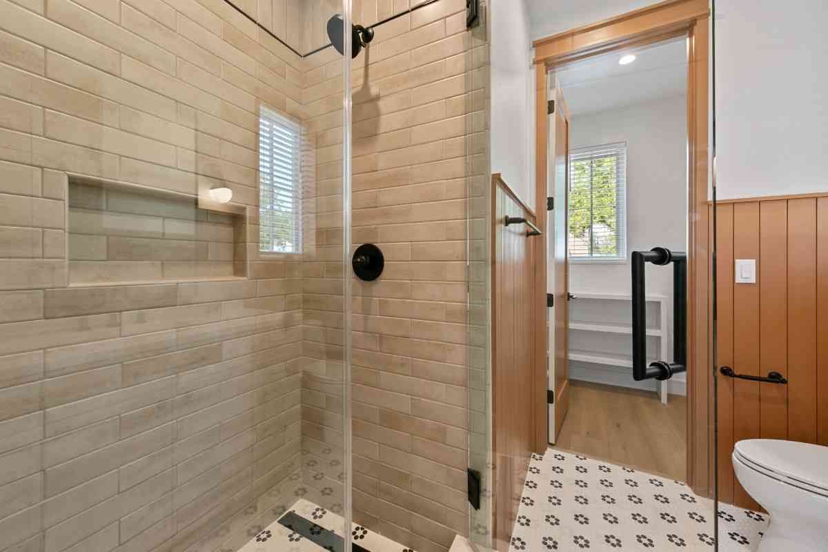 Bathroom with tiled shower, glass door, open door to toilet, wood floor, and white walls.