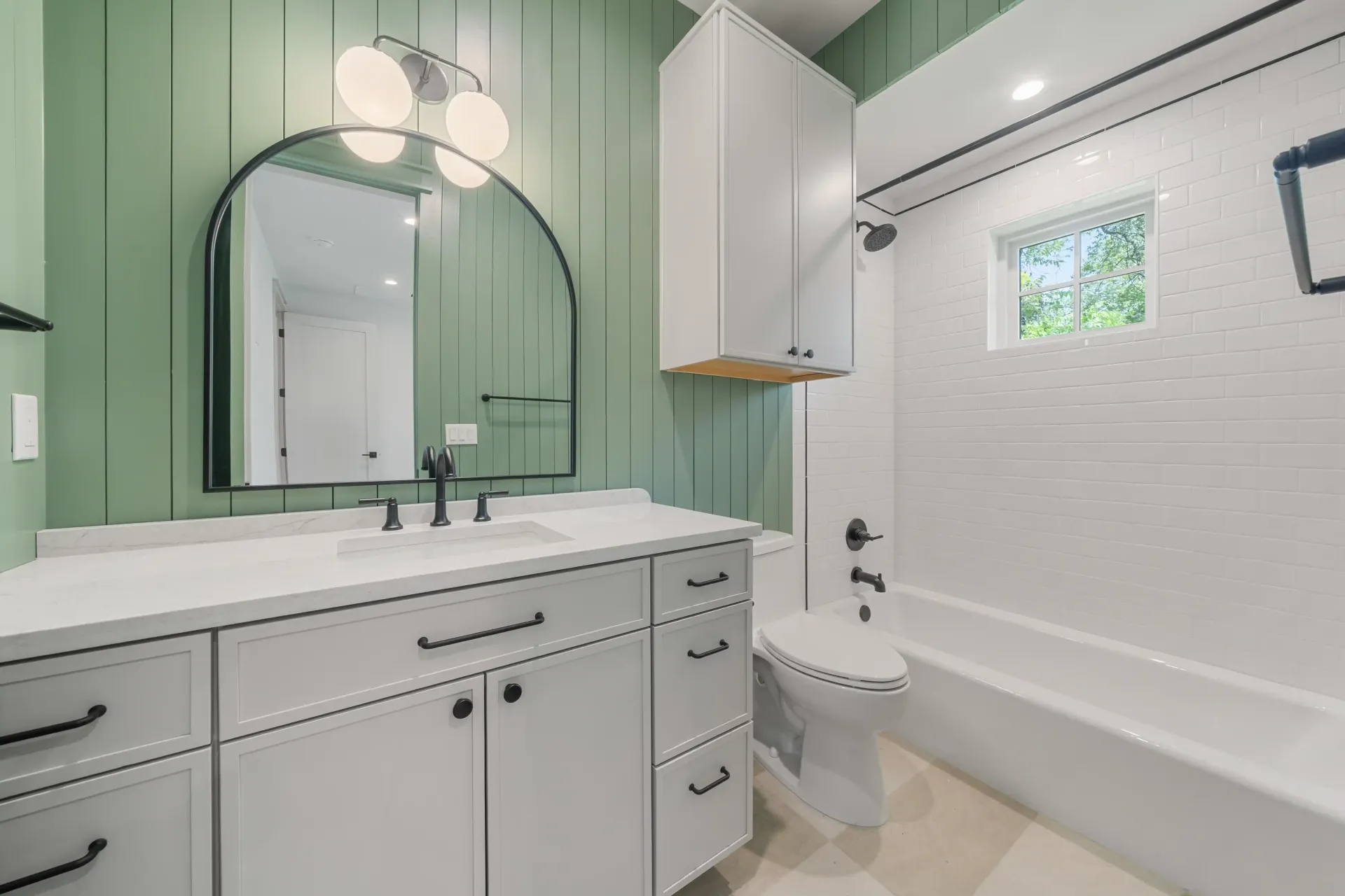 Bathroom with white vanity, green wall, black mirror, and white tiled bathtub.