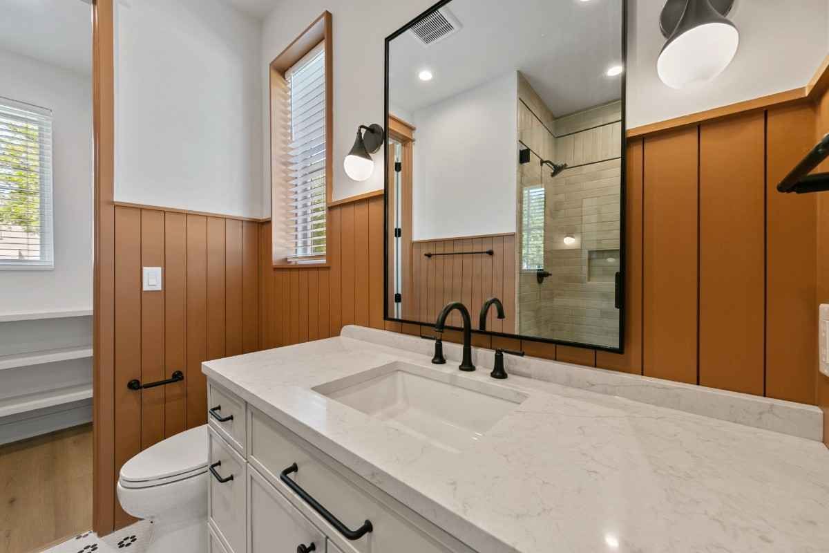 Bathroom with white vanity, brown paneling, black faucet, and large mirror.