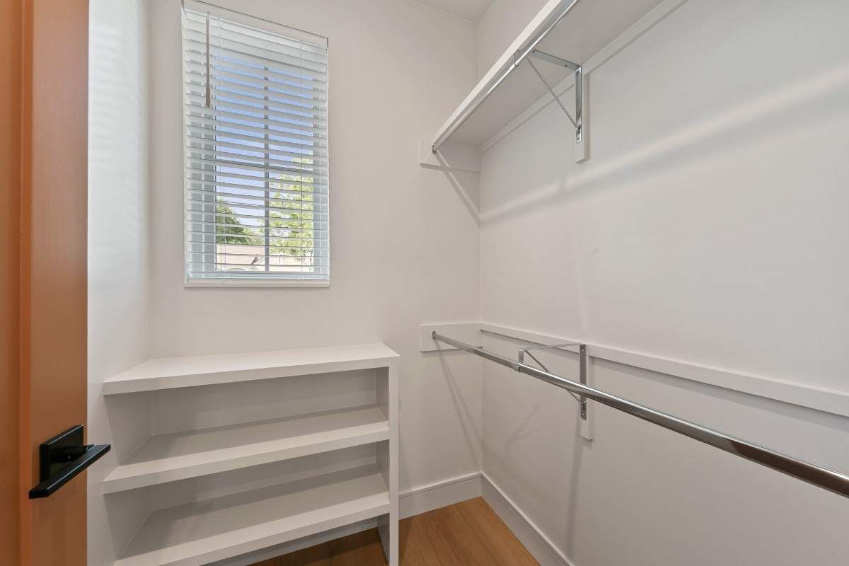 Empty white walk-in closet with shelves, a hanging rod, and a small window with blinds.