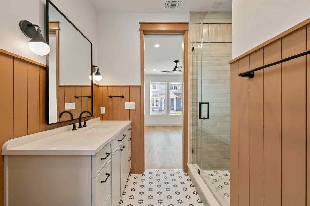 Bathroom with white vanity, black hardware, brown paneled walls, and a glass shower.