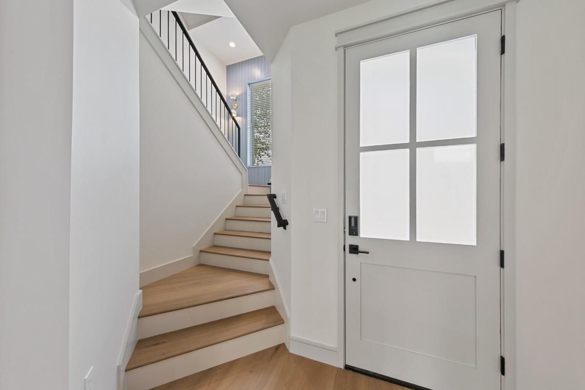 Interior entryway with stairs and white door. Wooden steps lead upwards, light floods in.