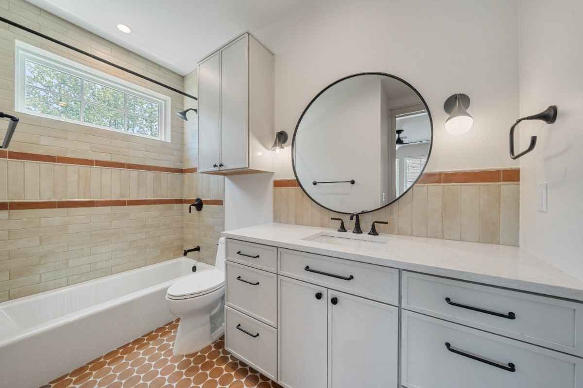 Bathroom with white cabinetry, round mirror, and tile accents.