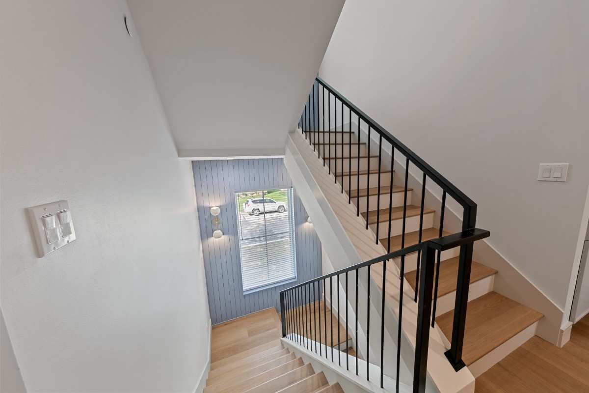 Staircase with light wood steps, black metal railing, and a window at the landing.