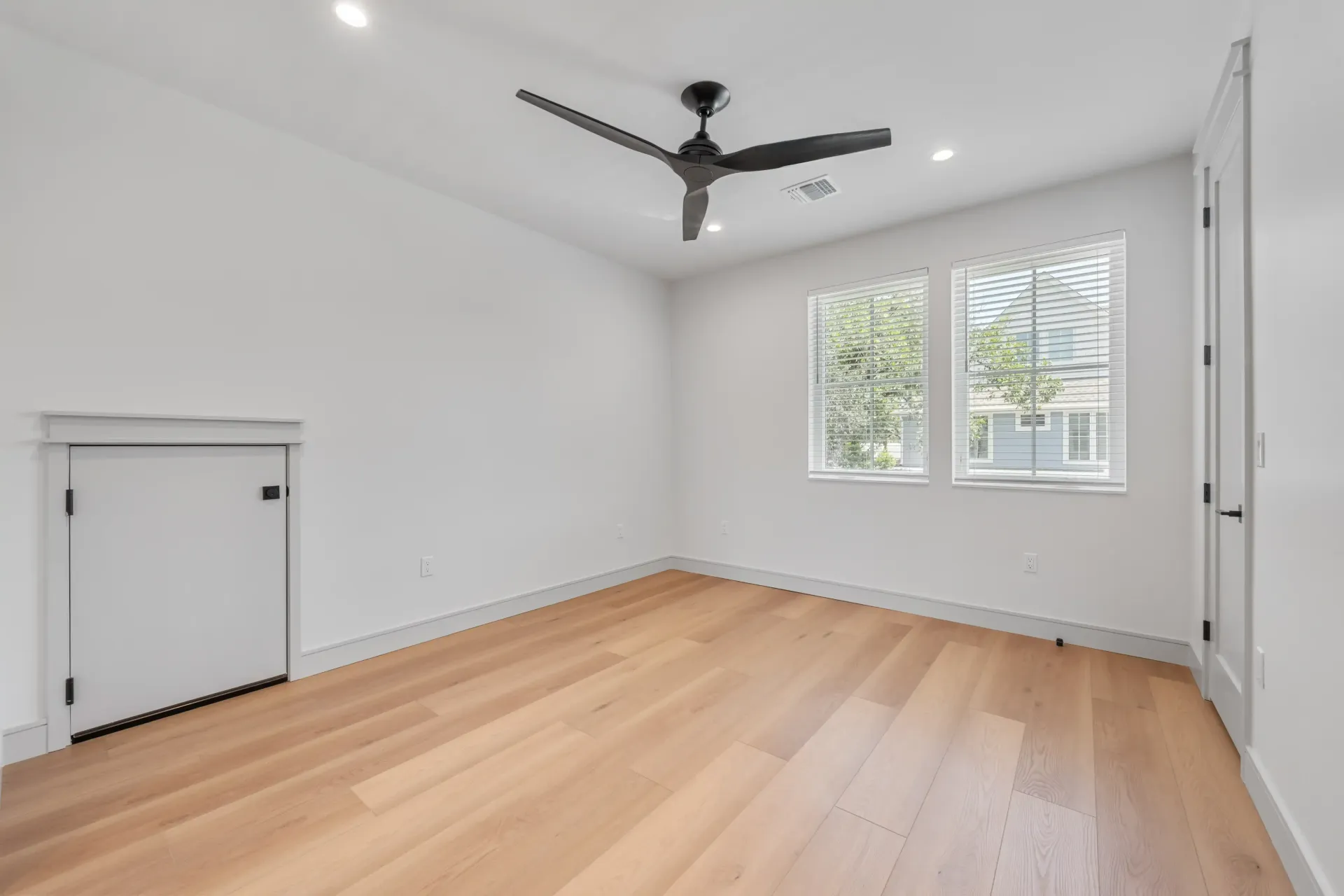 Empty room with hardwood floors, two windows, and a black ceiling fan.