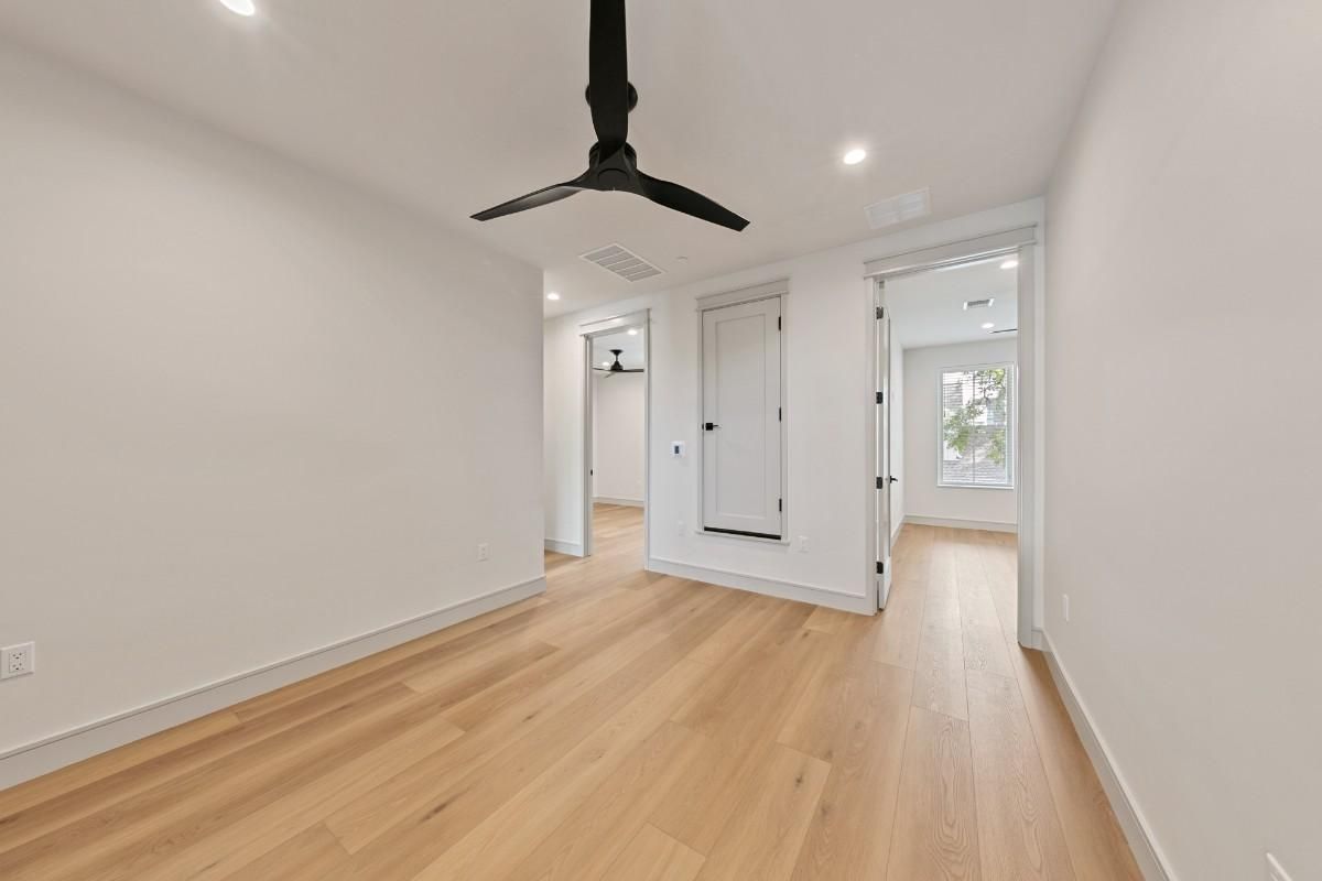 Empty room with hardwood floors, white walls, and a black ceiling fan. Two doorways lead to other rooms.