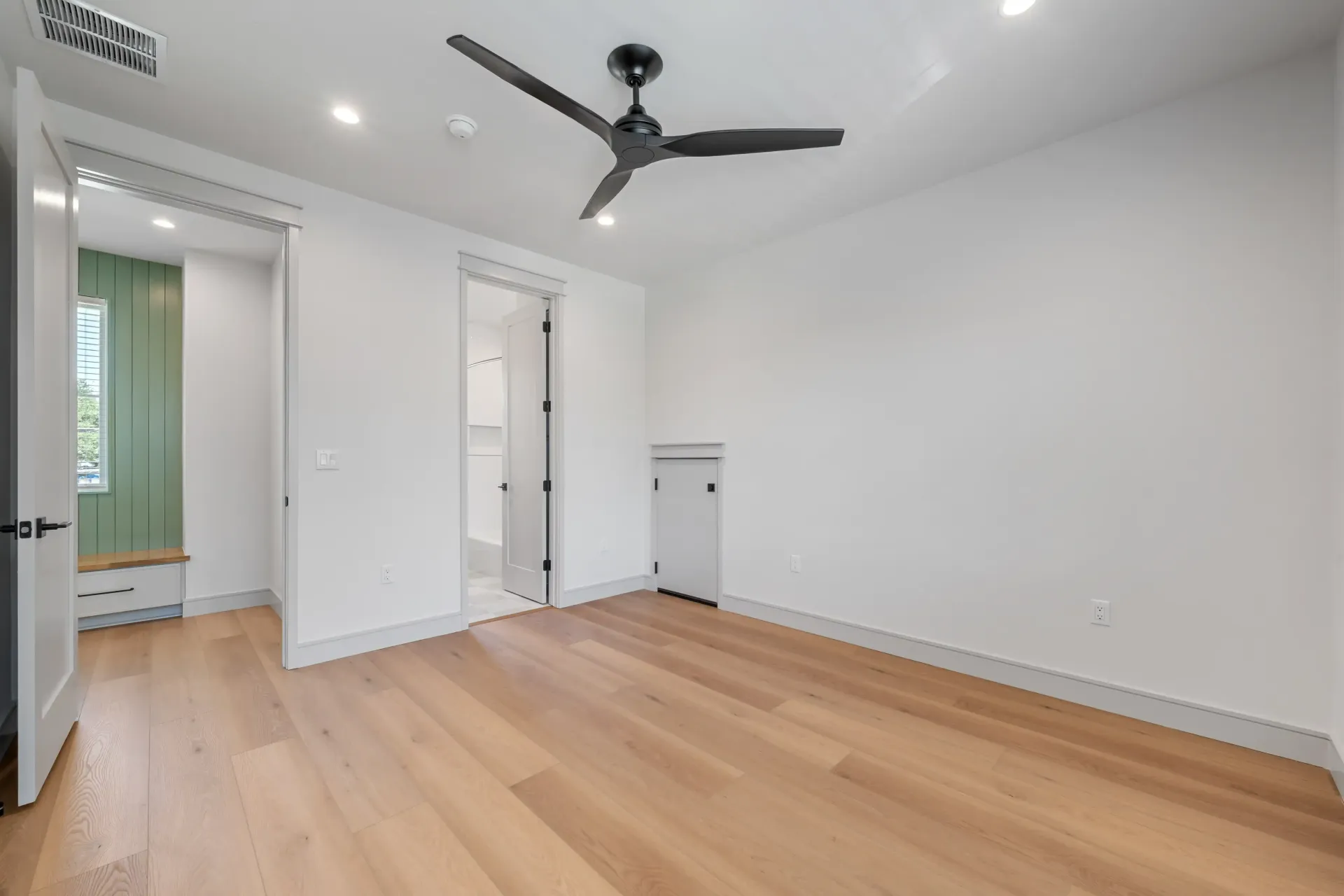 Empty room with light wood floors, white walls, and a black ceiling fan.