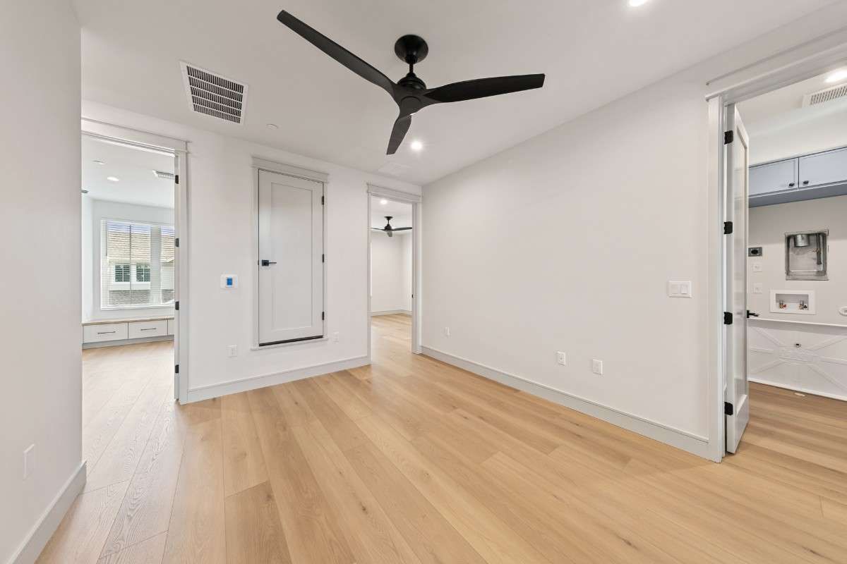 Empty room with hardwood floors, white walls, black ceiling fan, and doorways.