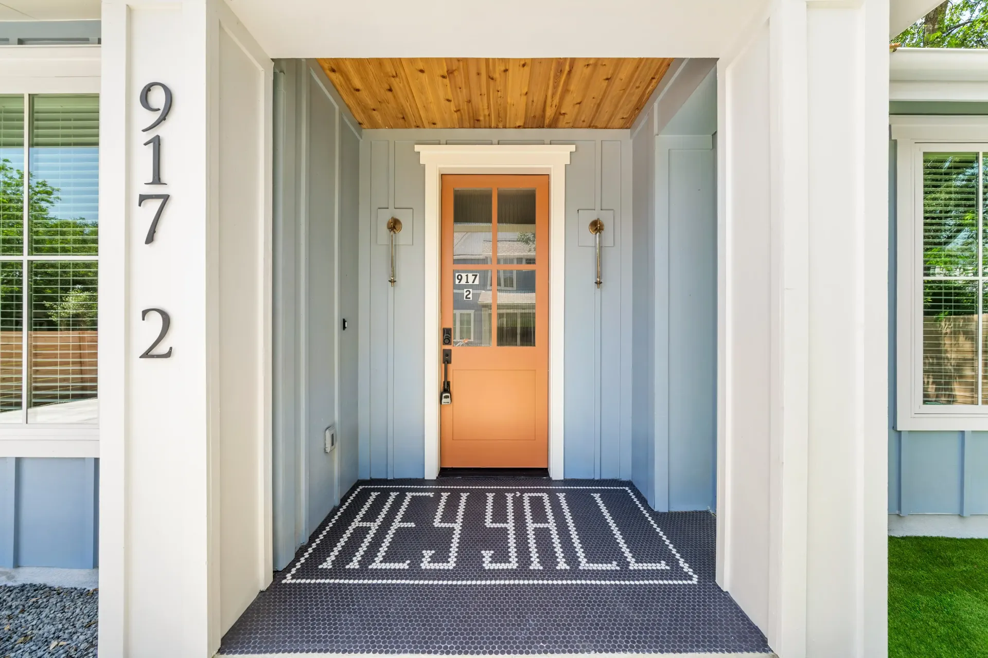 Entryway of a house with light blue siding and a tan door; mat reads 