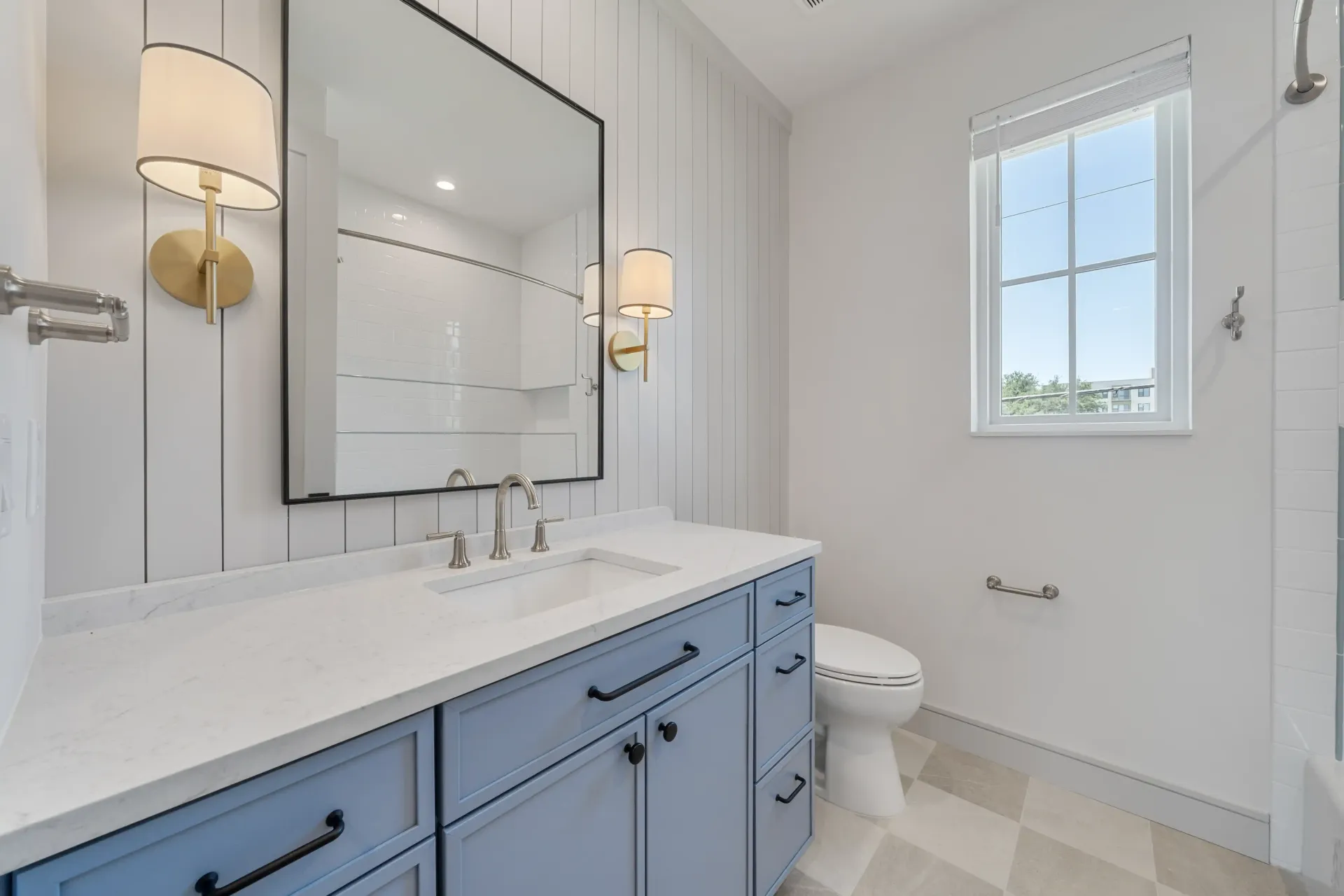 Blue vanity bathroom with white walls, gold sconces, and a large mirror.