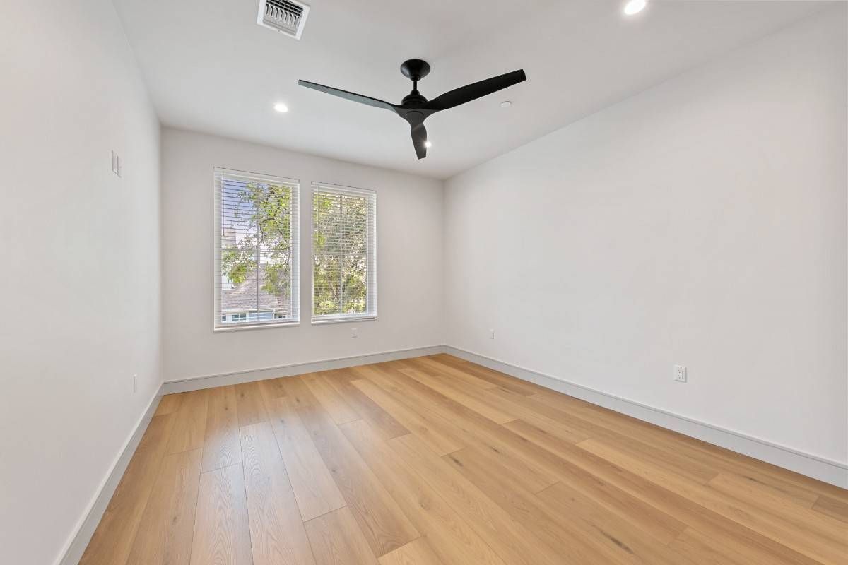 Empty room with hardwood floors, white walls, two windows, and a black ceiling fan.