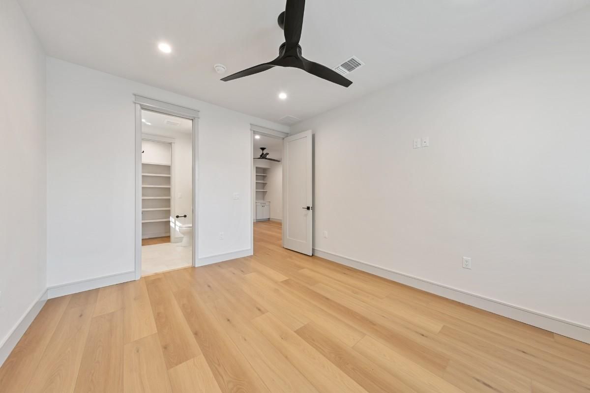Empty bedroom with wood floors, white walls, and a black ceiling fan; walk-in closet visible.