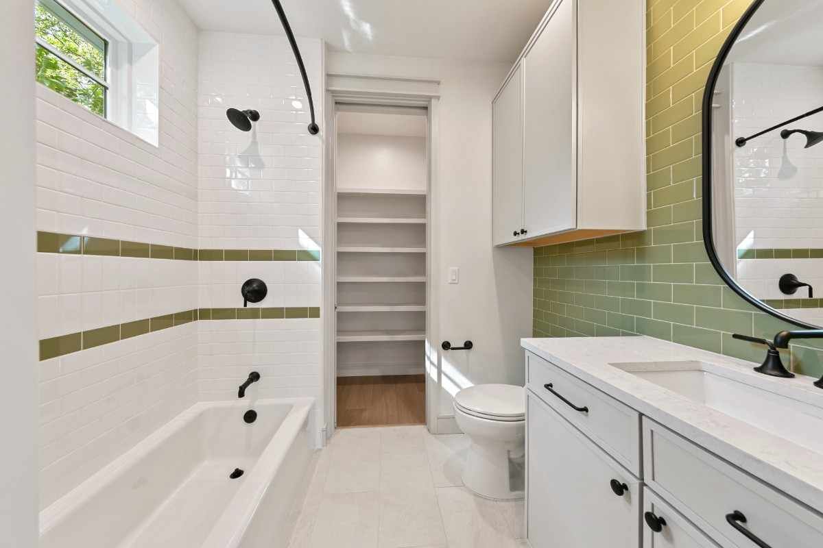 Bathroom with white and green tile, black fixtures, and a tall storage closet.
