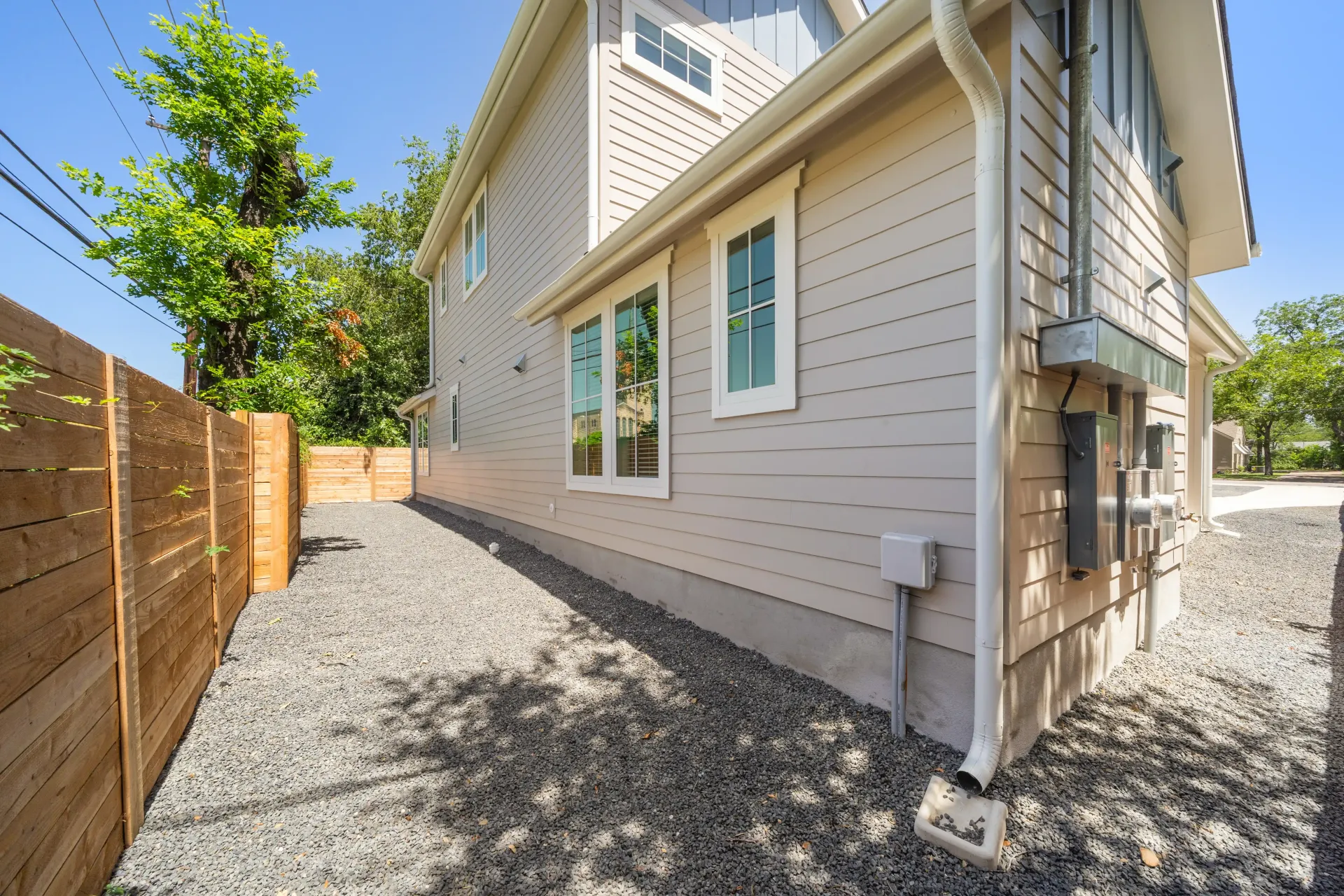 Exterior of a two-story beige house with a gravel walkway and wooden fence.