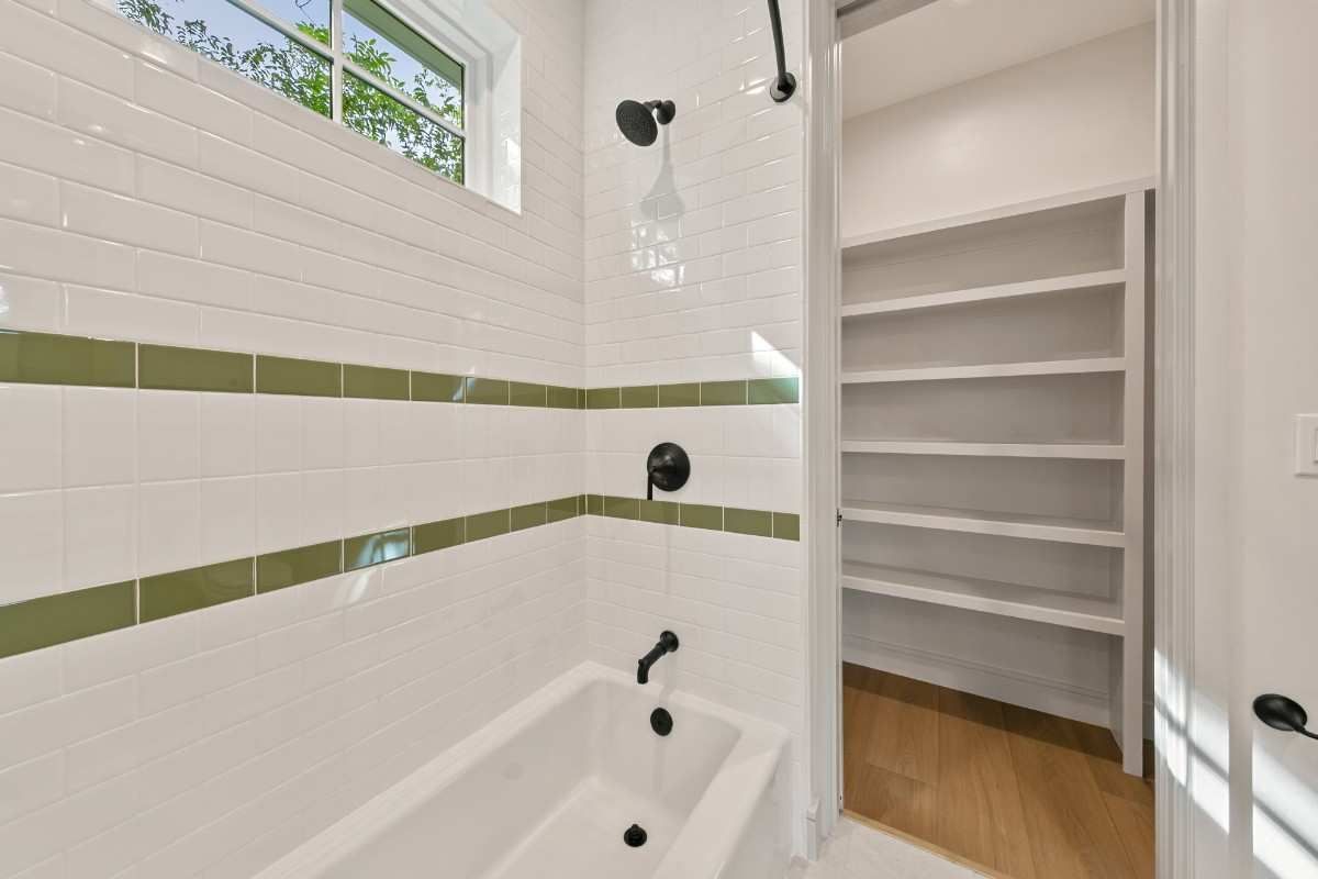 Bathroom with white tile, olive green stripe, black fixtures, and a walk-in closet.