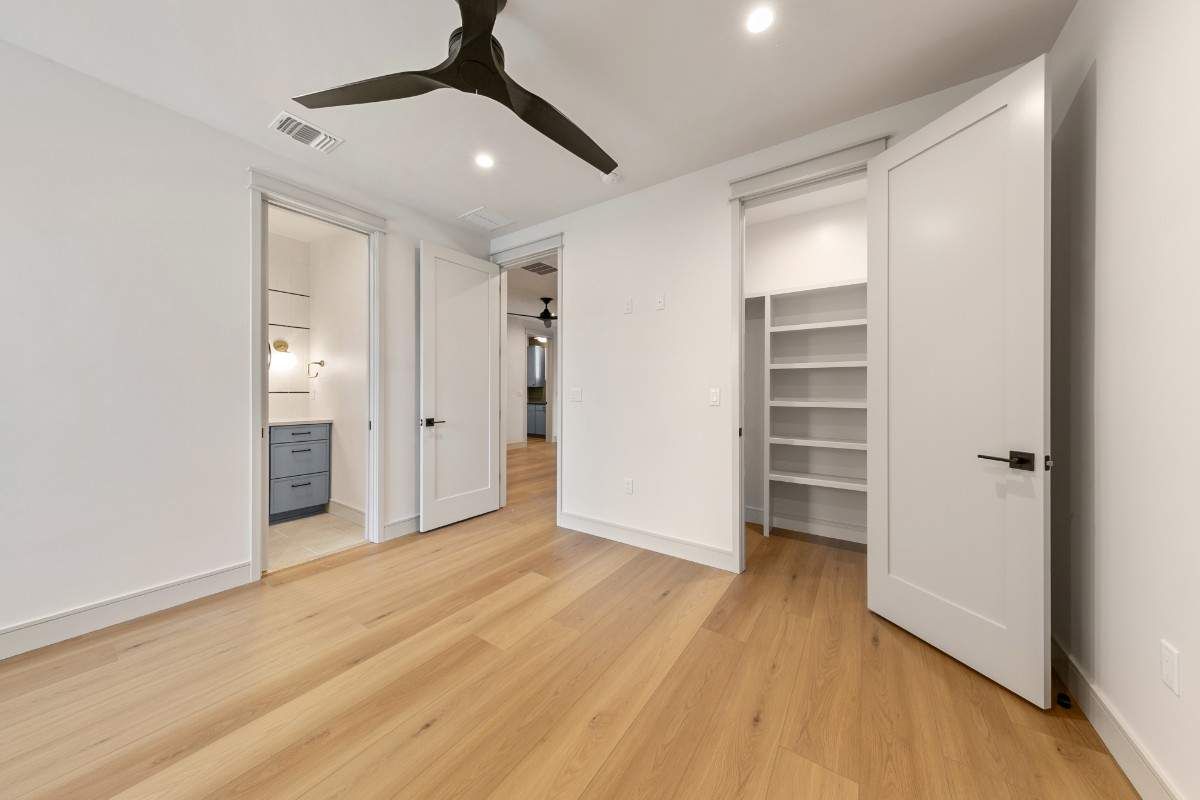 Empty bedroom with hardwood floors, white walls, and open doors to a bathroom and closet.