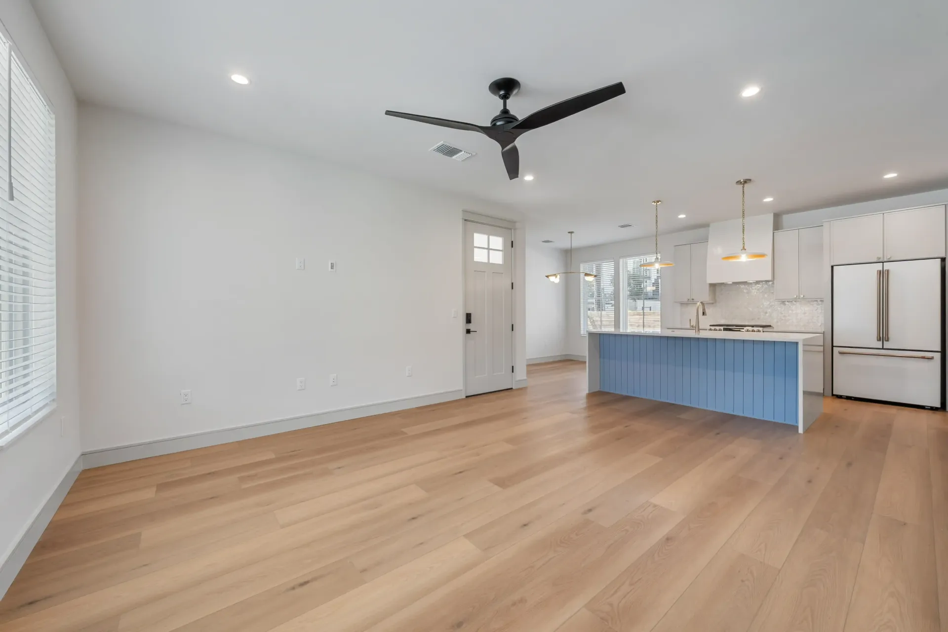 Open-concept living space with light wood floors, a blue kitchen island, and white walls.