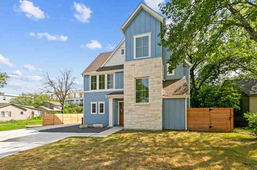 Blue and stone two-story house with brown roof and wooden fence in a grassy yard.