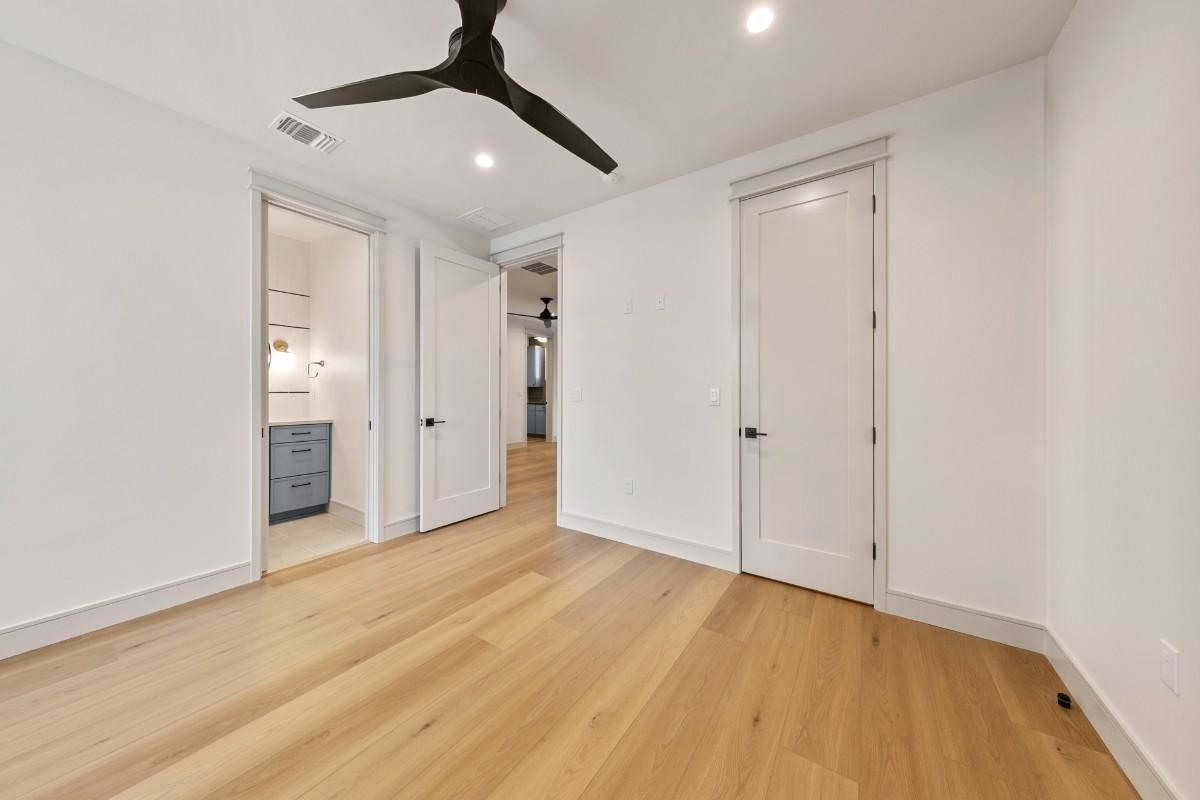 Empty room with light wood floor, white walls, and three white doors; one opens to a bathroom.