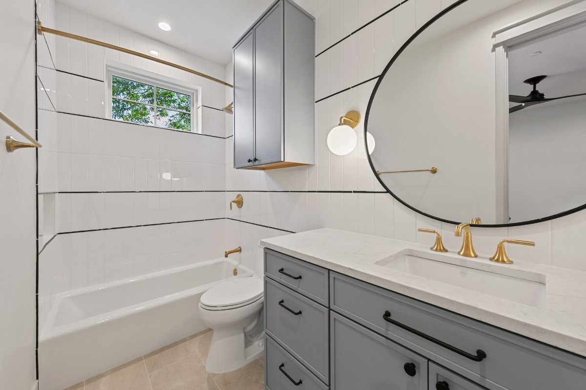 Gray and white bathroom with a round mirror, gold fixtures, and a gray vanity.