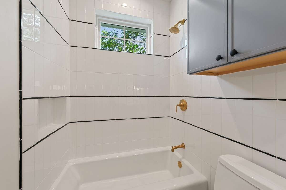 White bathroom with bathtub, gold fixtures, and a window.