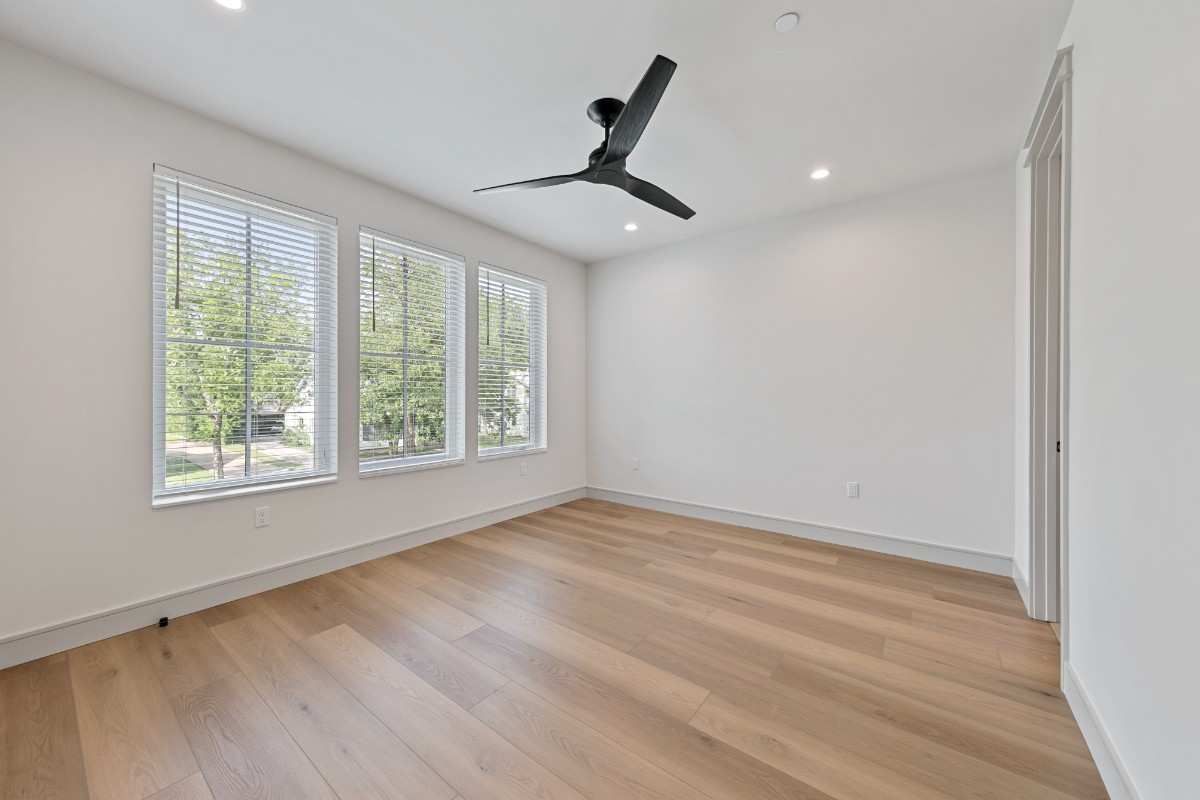 Empty room with three windows, hardwood floors, and ceiling fan.