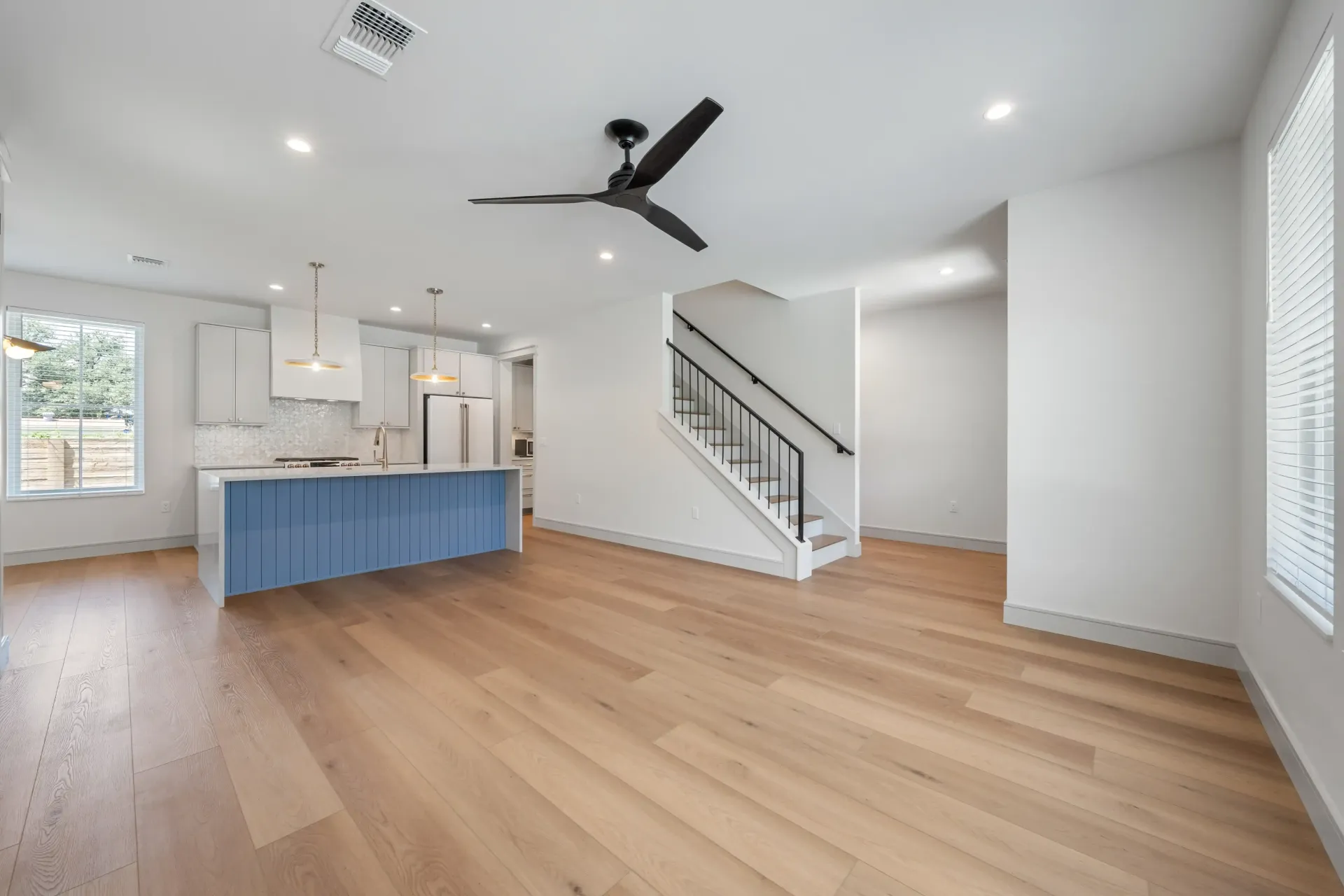 Spacious, modern living area with blue kitchen island, light wood floors, and stairs.
