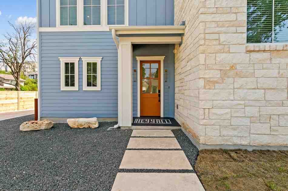 Blue and stone exterior with brown door, concrete walkway, and gravel landscaping.