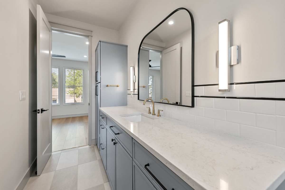 Bathroom with blue cabinets, white countertop, black-framed mirror, and modern sconces.