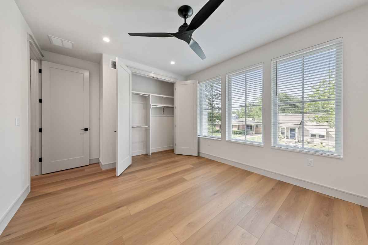 Bedroom with hardwood floors, white walls, closet, windows with blinds, and ceiling fan.