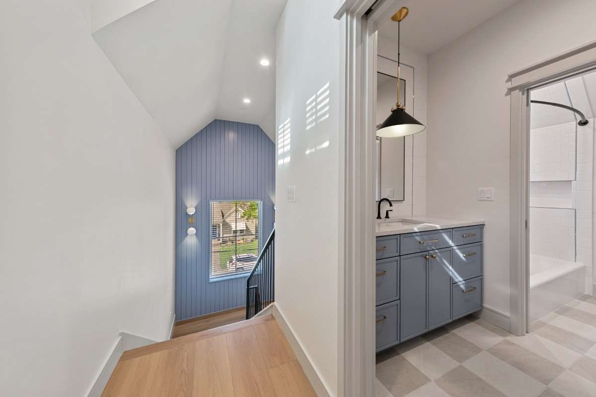 Hallway with blue paneled wall, stairs, and bathroom with blue vanity.