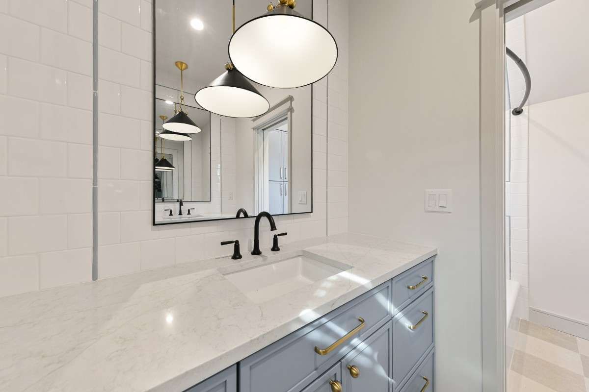 Bathroom with blue vanity, white countertop, black faucet, and pendant lights.