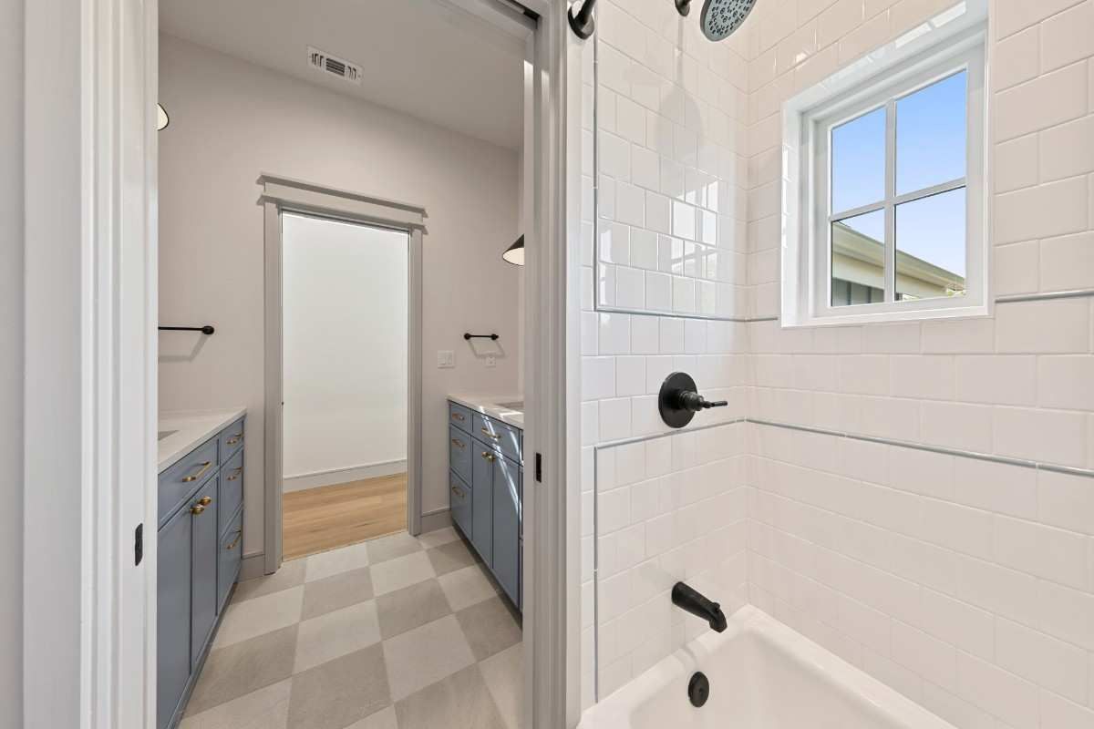 Bathroom with glass shower, blue cabinets, checkered floor, and a window with a view of a building.