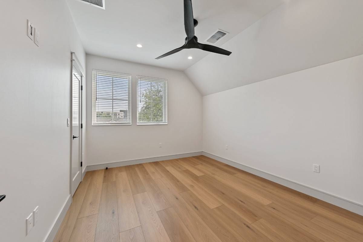 Empty room with light wood floors, white walls, black ceiling fan, and window with blinds.