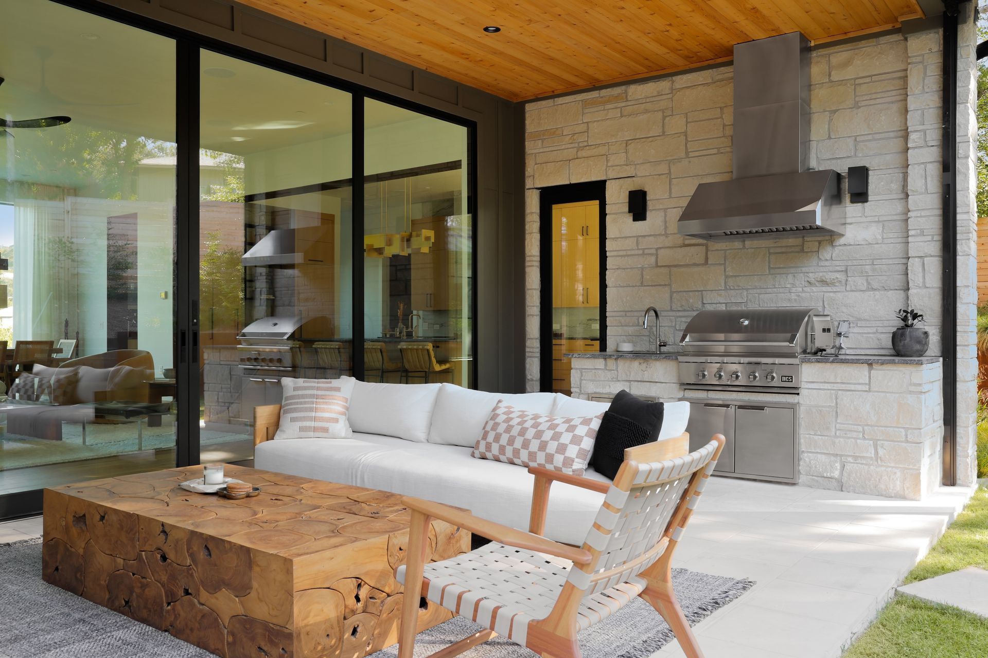 Outdoor kitchen with seating area: white couch, stone wall, grill, and wooden table.