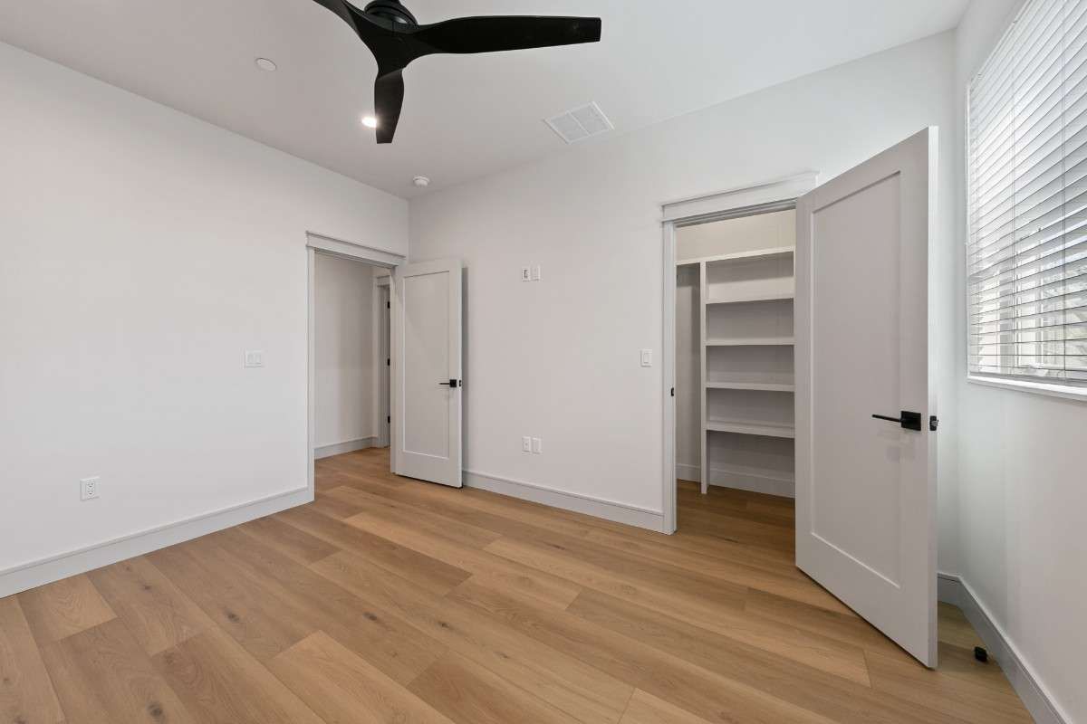 Empty bedroom with wood flooring, white walls, closet, and a ceiling fan.