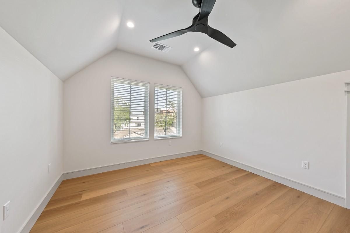 Empty room with light wood floor, white walls and ceiling, two windows, and a ceiling fan.