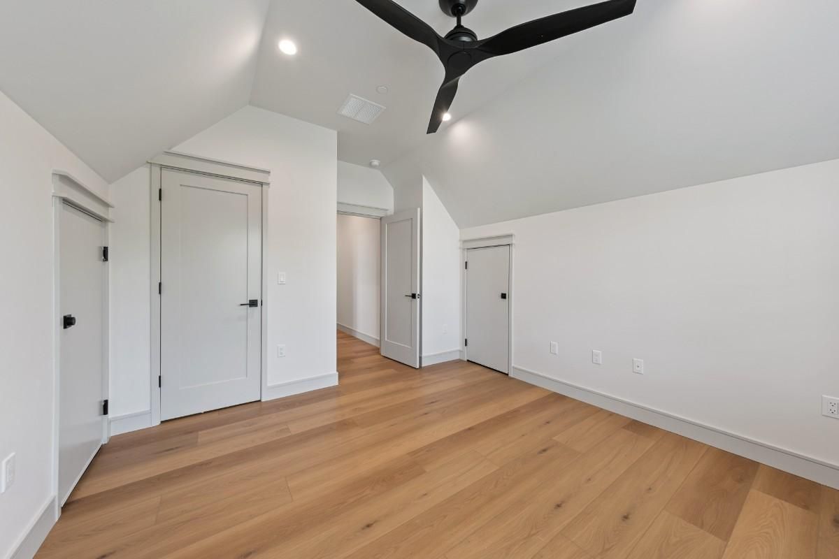 Empty room with hardwood floors, white walls, multiple doors, and a black ceiling fan.