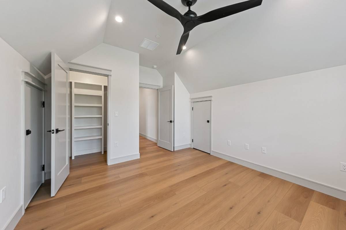 Empty bedroom with hardwood floors, white walls, and a black ceiling fan.