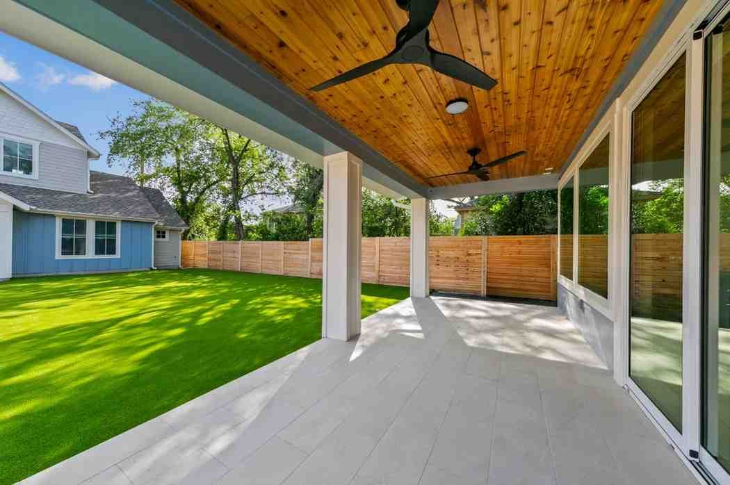 Covered patio with a wood ceiling, overlooking a backyard with green grass and a wooden fence.