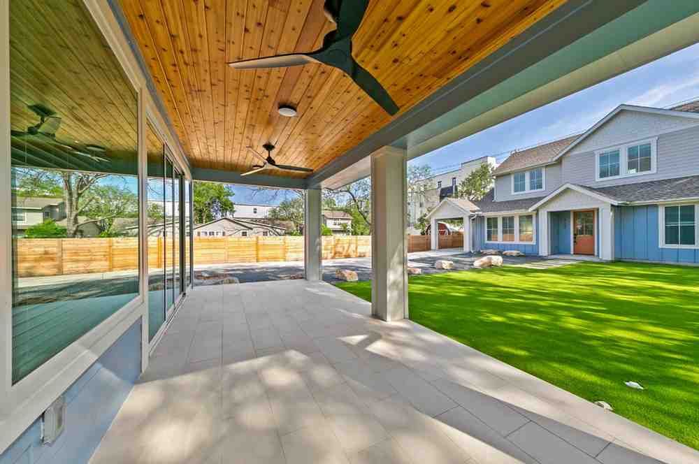 Covered patio with wood ceiling, tile floor, glass walls, and view of a house and yard.