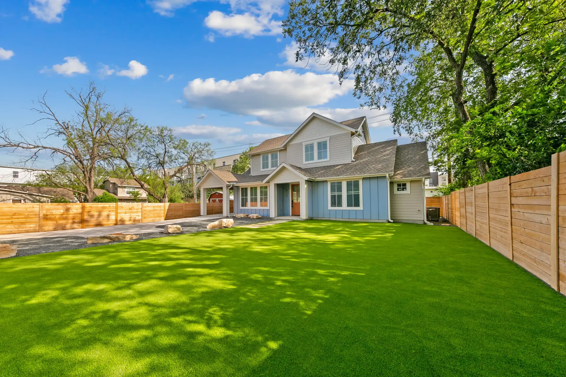 Two-story house with blue and gray siding, green lawn, and wooden fence on a sunny day.