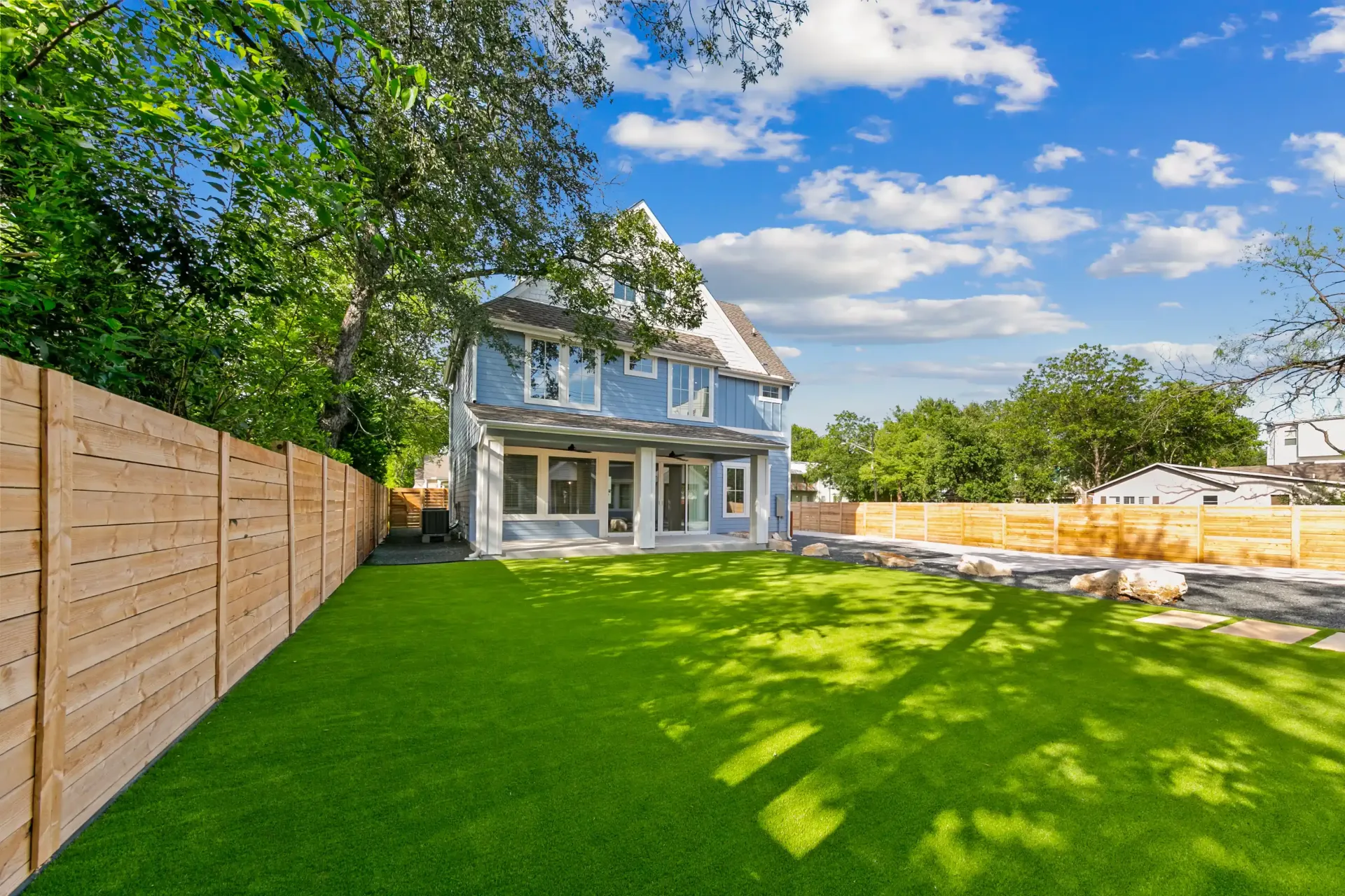 Blue house with large backyard, green grass, wooden fence, and sunny sky.