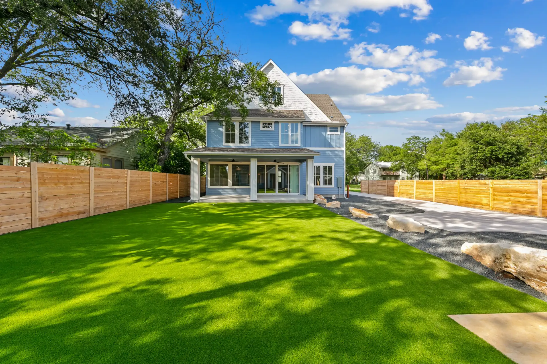 Blue house with green lawn, wooden fence, and blue sky.