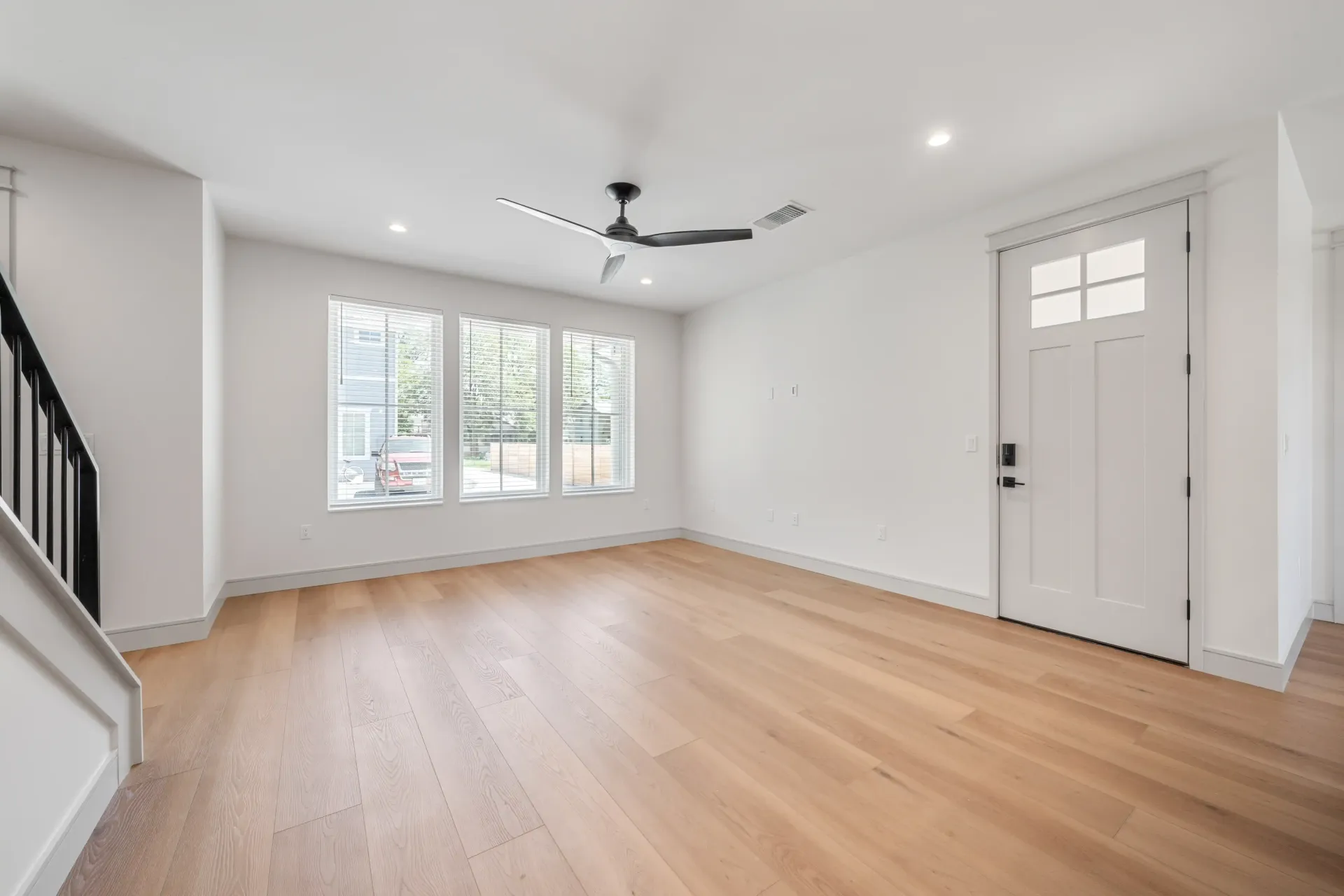 Empty modern living room with hardwood floors, white walls, and a black ceiling fan.