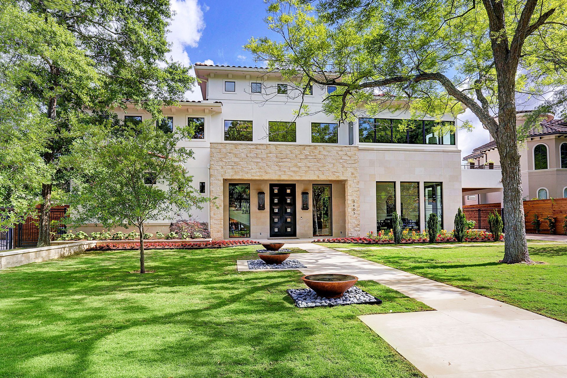 Modern two-story house with stucco exterior, stone accents, and manicured lawn.